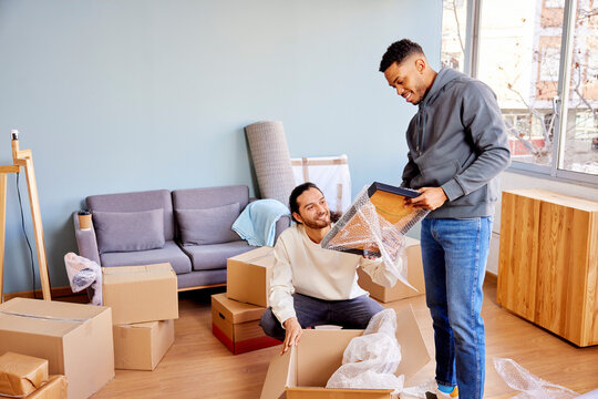Smiling multiracial men in casual clothes unpacking picture