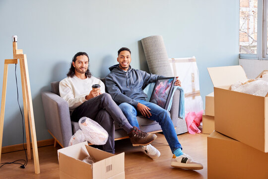 Positive diverse male friends sitting on gray sofa with a coffee