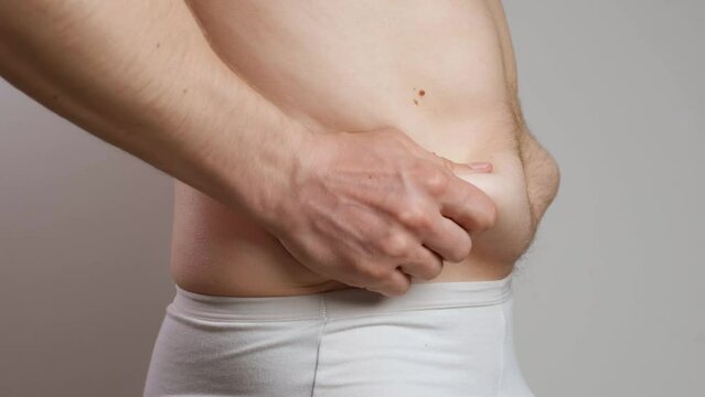 Men's hands touch the excess fat hanging on the sides of the abdomen. The concept of overweight, overeating and malnutrition