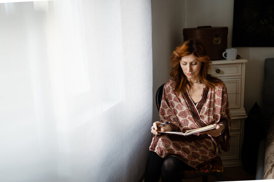 A woman reads near a window in the bedroom