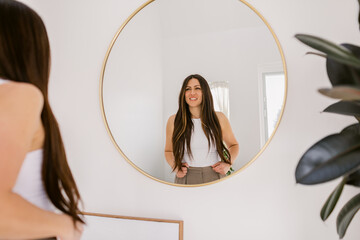 Happy woman looks at herself in mirror at home