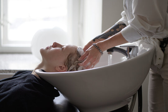 Crop hairstylist washing hair of client in salon