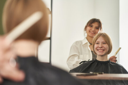 Cheerful female client enjoying haircut in salon mirror