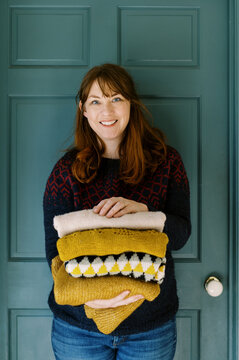 Happy smiling woman holding stack of handmade knit sweaters