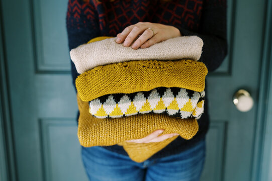 Happy smiling woman holding stack of handmade knit sweaters