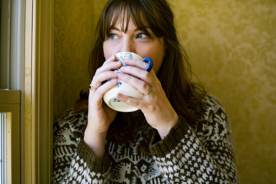 Woman relaxing and drinking coffee by the window from a mug