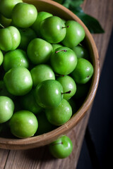 Fresh green plums in a bowl on dark background.