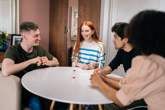 Laughing multiethnic friends having play cards games for time, enjoying board games activity for entertainment at home. Cheerful diverse men and women playing UNO board game sitting at table.