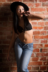 Fototapeta na wymiar sensual asian beauty in black bra and jeans smoking a cigar against a wall