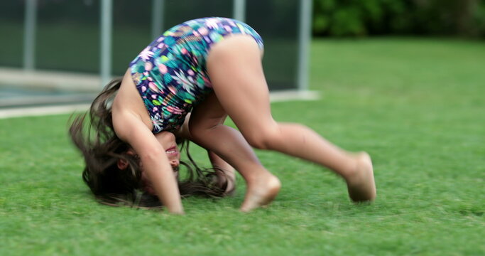 Child girl doing somersault outdoors. Little kid tumbling outside in grass