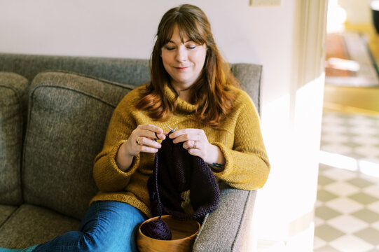 Happy Relaxed Woman Sitting On Sofa In Her Home And Knitting