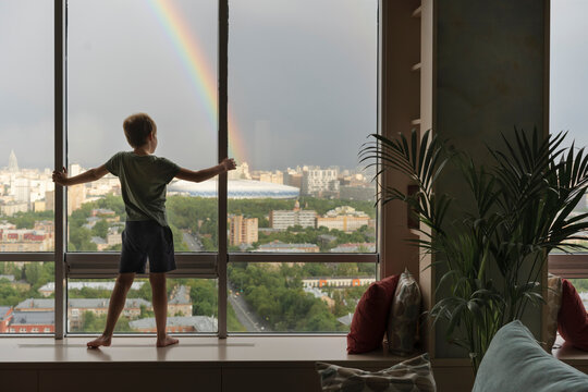 Kid admires view of rainbow  from large window.