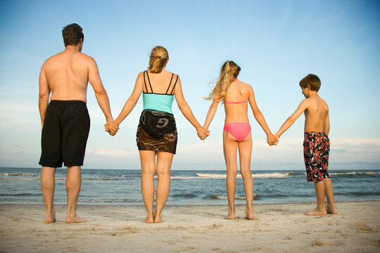 Rear view of a family holding hands at the beach. Horizontal shot.
