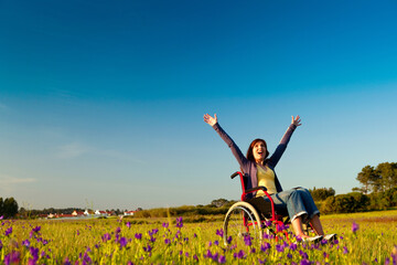 Happy handicapped woman on a wheelchair over a green meadow