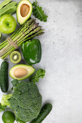 Healthy vegetarian food: green vegetables and herbs on a gray background. Top view. Assorted green vegetables: broccoli, beans, avocado, zucchini, kiwi, asparagus. Alkaline diet. 