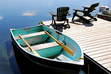 Two wooden adirondack chairs on a boat dock on a beautiful still lake with sky reflection