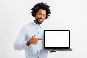 Smiling positive african-american man holding laptop with empty screen and pointing finger on it standing isolated on white background, advertising new app or offer