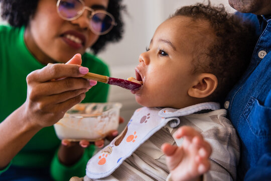 Cheerful black mother and feeding little son with puree