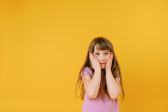 Happy cute toddler girl wearing violet shirt on yellow background