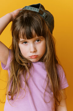 grumpy sad little toddler girl wearing hat and violet shirt on yellow