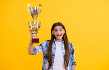 amazed teen girl receive award in studio. teen girl accept award on background. proud teen girl with champion cup award. teen girl hold her award champion cup isolated on yellow