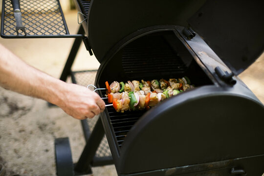 man grilling chicken shish kebab skewers on the bbq grill