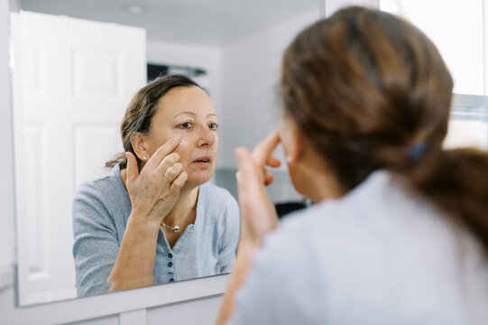 woman putting lotion on face for self care in bathroom