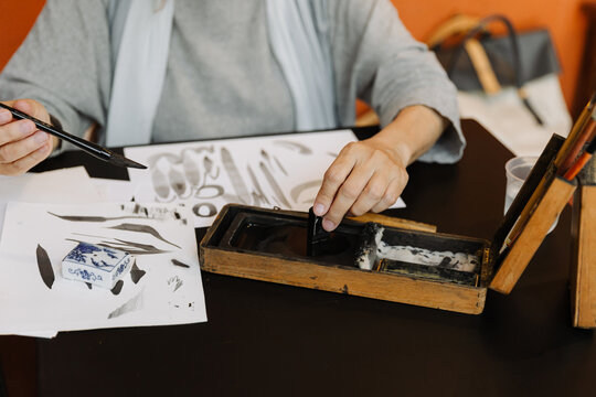 Senior woman using ink stick during calligraphy lesson