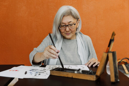 Senior woman dipping brush into ink