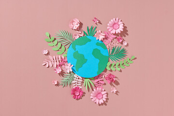 Globe with paper colorful flowers and leaves on a pink background.