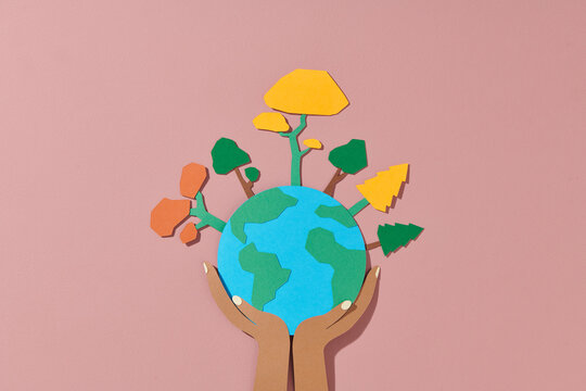 earth with plants over hands paper cut on color background