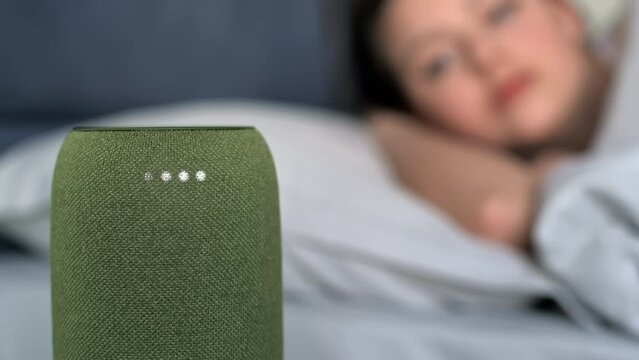 A sleeping woman turning off alarm clock on a portable wireless speaker with 4 luminous diodes