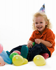 Adorable little three year old boy wearing party hat sitting with balloons with happy expression