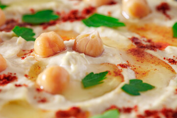 Hummus with chickpea grains red pepper olive oil and herbs close-up, selective focus