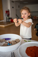 Little girl playing with kinetic sand and toys insect. Sensory development and experiences, themed...