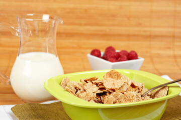 A bowl of cornflakes, milk and raspberries on bamboo mat
