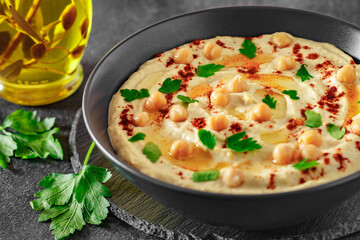 Hummus with chickpeas and olive oil in a dark bowl, on slate stone plate round, selective focus
