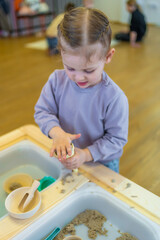 Little girl playing with kinetic sand and wooden toys. Sensory development and experiences, themed...