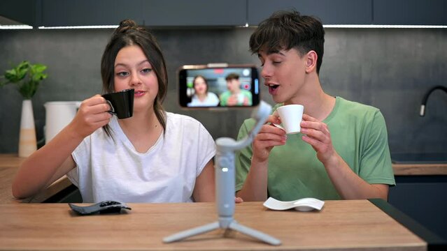 Young smiling man and woman blogger influencers talking and shooting themselves on smartphone on a stabiliser in a kitchen