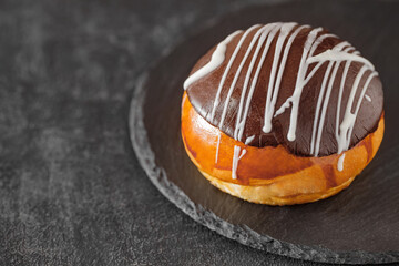 Bun with chocolate chip and white stripes of glaze, on slate stone plate round, dark background, selective focus