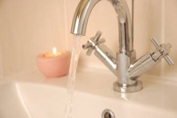tap running into washbasin with candle in background