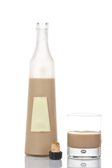 A whiskey cream bottle and glass with ice cubes, reflected on white background