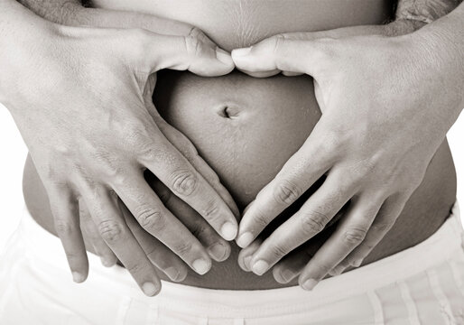 Pregnant women wrap her arms around the belly in the form of the heart. Isolated on white.