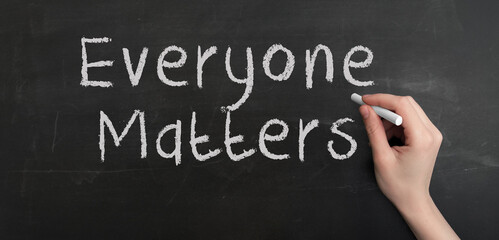 A woman's hand write text Everyone matters with chalk on chalkboard