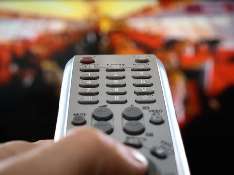 closeup of a hand  holding the remote control in front of the television, shallow DOF, conceptual image of the world under control