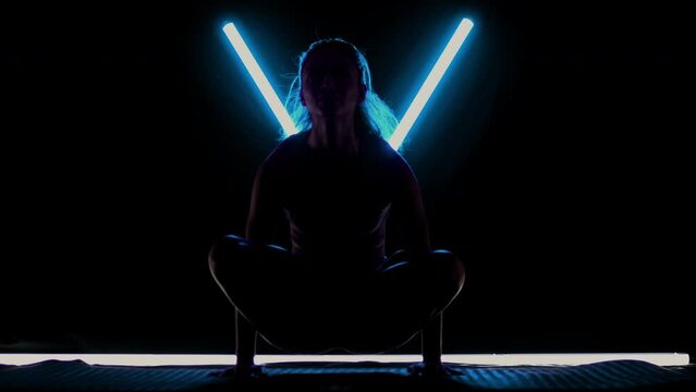 Fit woman practicing yoga poses. Silhouette girl doing exercise in studio against black background with v shaped blue led tube light. No stress inner balance concept..
