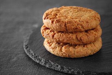 Oatmeal cookies three pieces stacked, on slate stone plate round, dark background, selective focus