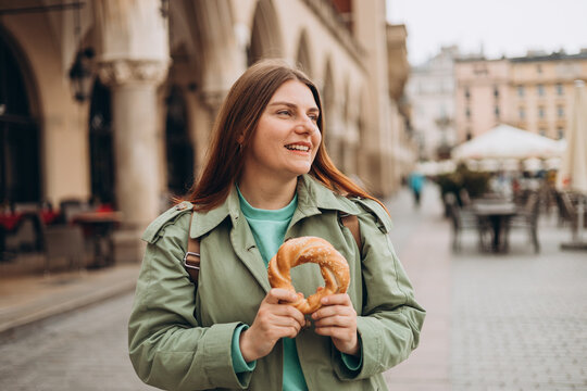 Attractive young female tourist is holding prezel, traditional polish snack on the Market square in Krakow. Traveling Europe in spring. Selective focus. High quality photo