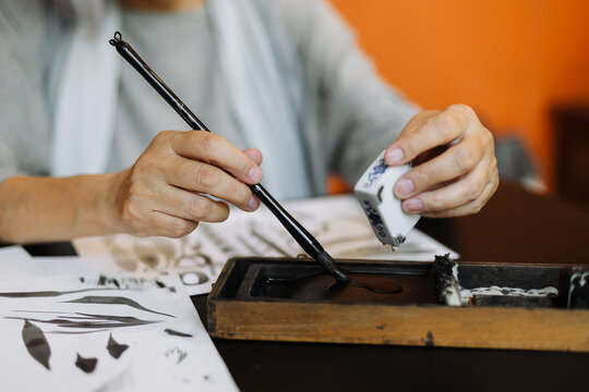 woman using ink stick during calligraphy lesson