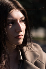 Portrait of a young and attractive Caucasian brunette girl on the street in autumn or spring in a coat